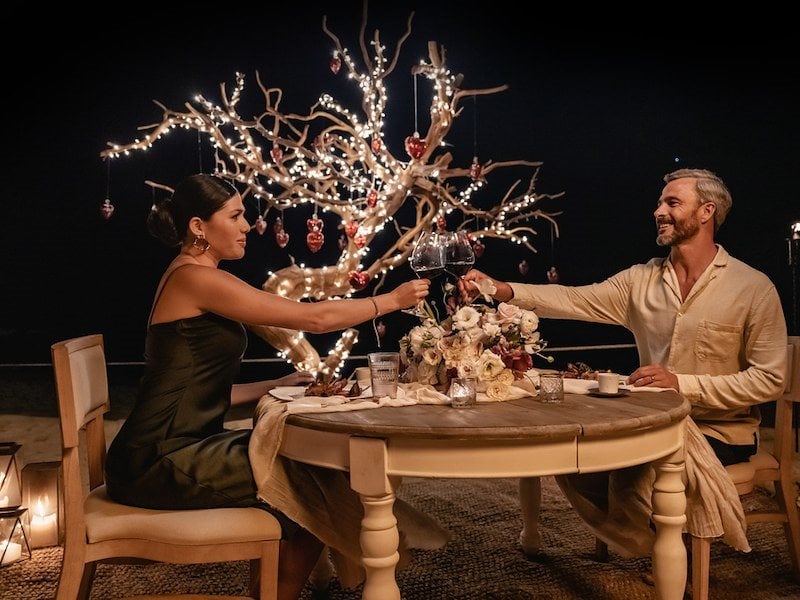 A man and woman sitting at a table with flowers and lights