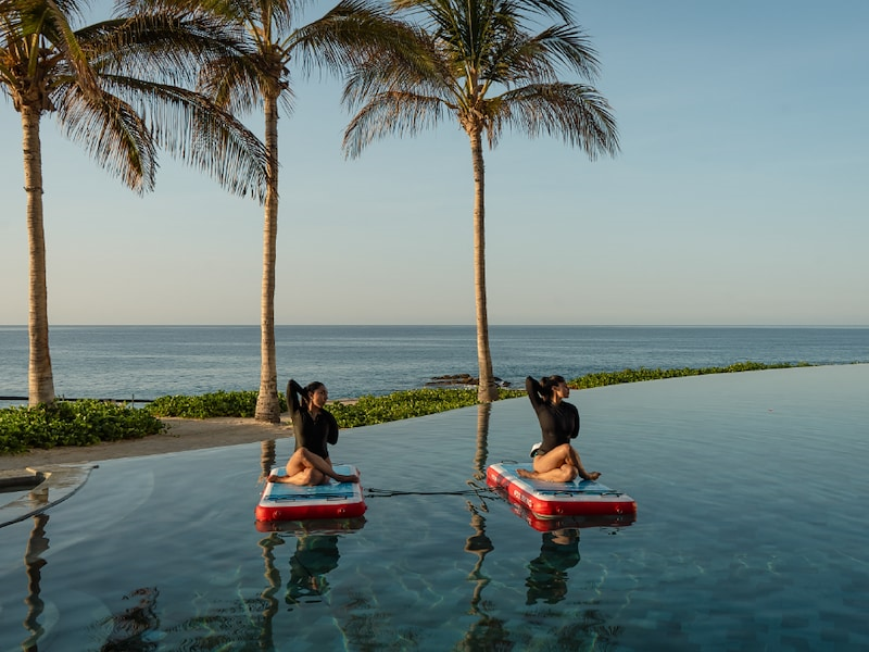 Two women on floating rafts in a pool with palm trees and water